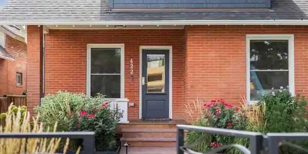 Image 2: A welcoming covered front porch is framed by lush landscaping and the homes original brick exterior.