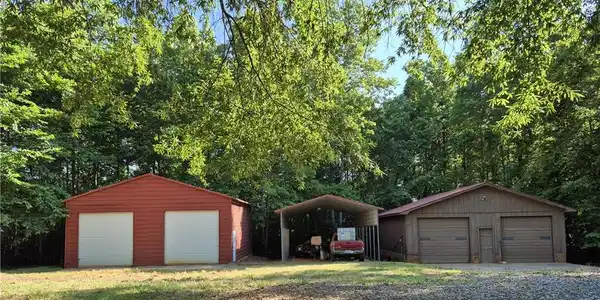 Image 4: Steel garage with side entrance, detached carport, workshop with woodburning stove and bathroom.