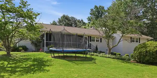 Image 4: Mature trees frame a charming home with well-kept